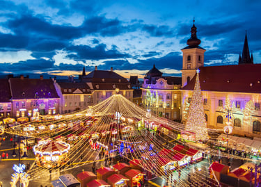 Sibiu Christmas Market at night featuring festive lights, a tall tree, and a carousel in the main square.