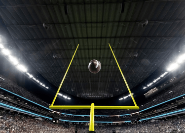 Low angle view of an American football flying through yellow goal posts in a crowded indoor stadium.