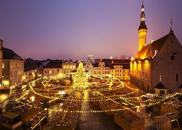 Tallinn Christmas market at dusk with glowing festive lights, a large tree, and historic town hall architecture.
