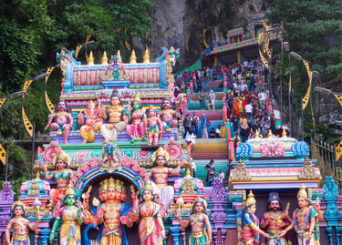 Colorful Hindu statues and tourists on the rainbow stairs at the Batu Caves temple in Malaysia.