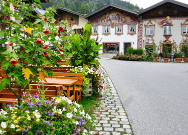 Charming Bavarian village street featuring traditional painted houses and an outdoor cafe terrace with flowers.