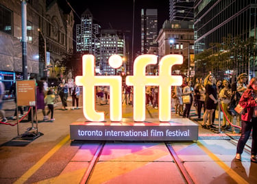 A glowing TIFF sign illuminates a crowded Toronto International Film Festival red carpet event at night.