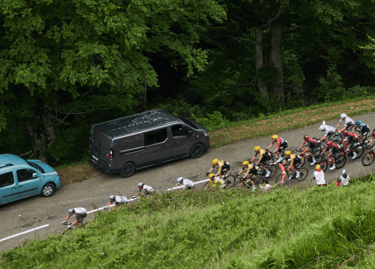 Professional cyclists racing in a peloton along a winding mountain road during a road cycling competition.