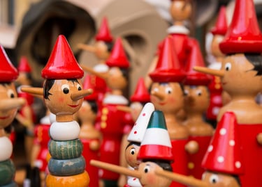 Handcrafted wooden Pinocchio dolls with red hats and long noses in an Italian souvenir shop.
