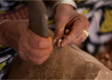 Woman opening an Argan nut with a stone without damaging the kernel inside.