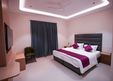 Modern hotel bedroom featuring a king bed with purple accents and ambient cove lighting.
