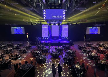 Grand gala ballroom setup with circular dinner tables, stage lighting, and large LED screens for an awards ceremony.