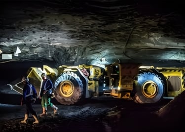 Dwaj górnicy idą obok ładowarki górniczej w kopalni