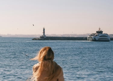 Donna seduta su una panchina al porto, di spalle, guarda il mare: vede traghetto e il faro