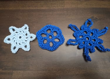three crochet snowflakes on a wooden table