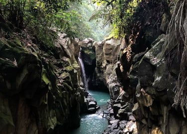 Kolam alami Curug Cikuluwung yang berwarna hijau kebiruan dikelilingi tebing batu sedimen vertikal dan sempit, menunjukkan pe