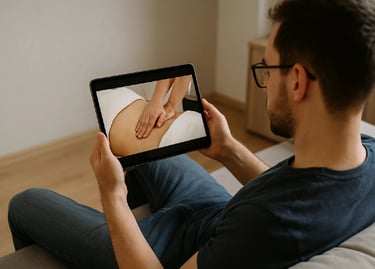Personne suivant une vidéo de massage abdominal sur une tablette, assise dans un salon.