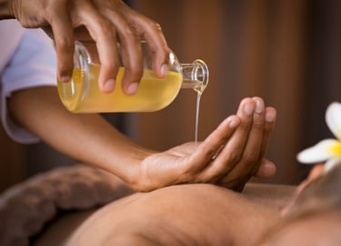 Thai aroma massage. A masseuse pores oil from into her hand above the bare back of a lady