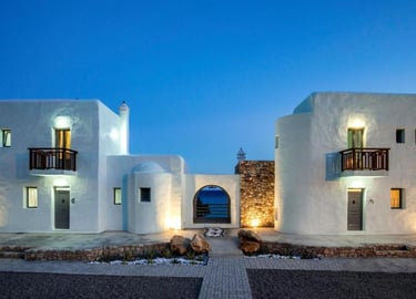 Luxury Cycladic villa in Rhodes at dusk with whitewashed walls and sea views through an archway.