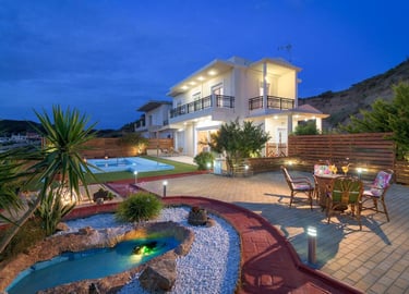 Luxury villa at twilight with a private swimming pool, garden pond, and outdoor dining area.