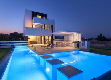 Modern luxury villa at dusk with a glowing blue infinity pool and outdoor patio.