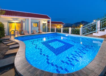 Luxury villa rental with a lit private swimming pool and red tile roof at twilight.