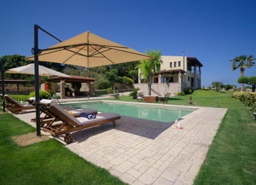 Luxury vacation villa with a private swimming pool, sun loungers, and patio umbrellas in a lush garden.