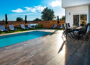 Luxury villa backyard with a swimming pool, sun loungers, and outdoor dining table.