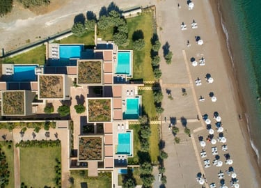Aerial view of a luxury beachfront resort with private pools and white umbrellas on a sandy shore.