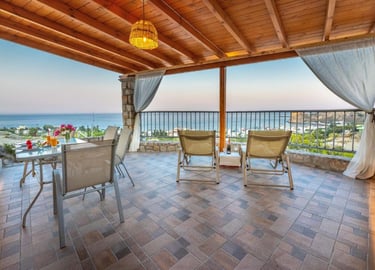 Luxury villa terrace with ocean views, outdoor dining table, and lounge chairs under a wooden pergola.
