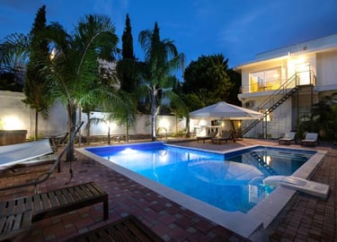 Luxury villa backyard with a lit swimming pool, palm trees, and lounge chairs at twilight.