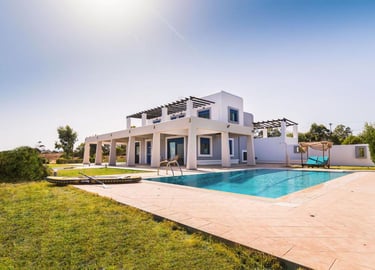 Luxury white villa with private swimming pool, sun lounge area, and green lawn under a clear sky.