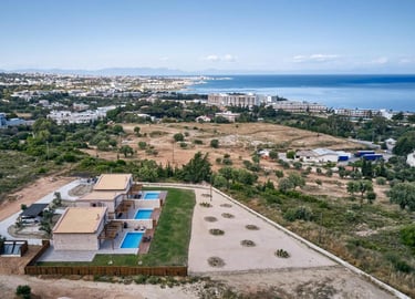 Aerial view of luxury holiday villas with private pools near the coastal shoreline in Greece.