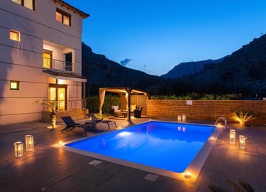 Luxury villa with an illuminated swimming pool and outdoor lounge at twilight in the mountains.