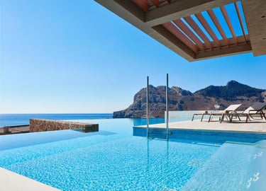 Luxury hotel infinity pool with ocean views, mountains, and lounge chairs on a sunny terrace.