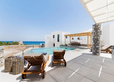 Luxury white villa with private infinity pool and sun loungers overlooking the blue ocean.