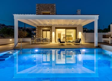 Luxury modern stone villa with a blue swimming pool and lit patio at night.