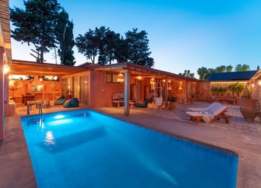 Luxury private villa with a glowing swimming pool, patio furniture, and rustic outdoor lounge at dusk.