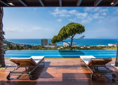 Luxury infinity pool with sun loungers on a wooden deck overlooking the blue ocean and resort skyline.