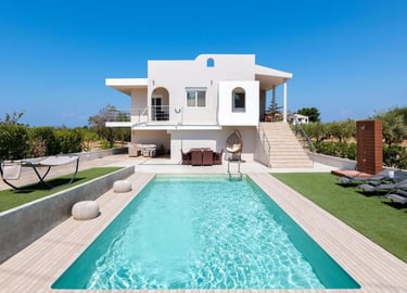 Luxury white villa with a private swimming pool, sun loungers, and outdoor patio under a clear blue sky.