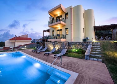 Luxury three-story villa with a lit swimming pool, sun loungers, and scenic views at dusk.