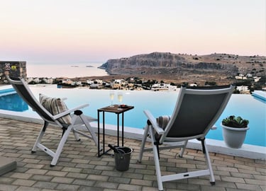 Luxury infinity pool terrace in Lindos, Rhodes with lounge chairs and ocean sunset view.