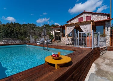 Luxury stone villa with a private swimming pool, wooden deck, and outdoor patio under a blue sky.