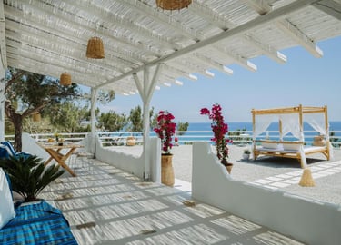 Luxury white beach resort terrace with canopy bed, rustic pergola, and sea view.