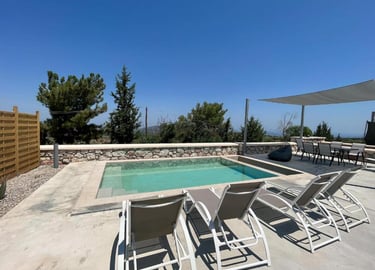 Luxury villa terrace with a private swimming pool, sun loungers, and outdoor dining area under a clear blue sky.