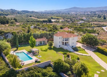 Aerial view of a luxury villa with a private swimming pool and garden in a Greek landscape.