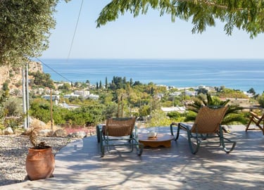 Luxury patio with outdoor lounge chairs overlooking the Mediterranean sea and coastal village.