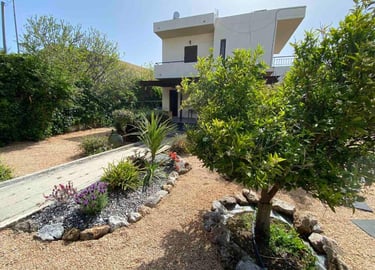 Two-story Mediterranean villa with a gravel courtyard garden and lush green trees.