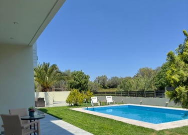 Luxury villa backyard featuring a private swimming pool, green lawn, and patio seating under a clear blue sky.