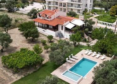 Aerial view of a Mediterranean villa with a swimming pool, sun loungers, and lush green gardens.