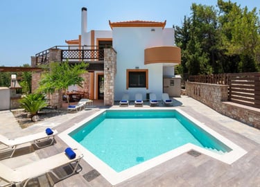 Luxury villa with private turquoise swimming pool, sun loungers, and stone patio area.