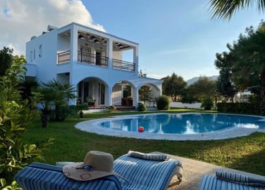 Luxury white villa with private swimming pool and sun loungers in a tropical garden setting.