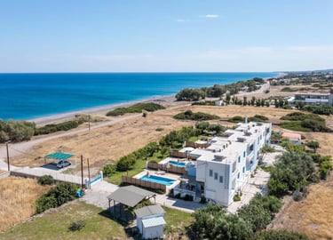 Aerial view of a luxury beachfront villa resort with private pools near a sandy Mediterranean beach.