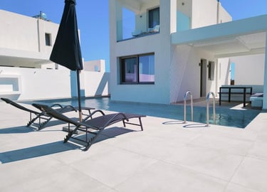 Luxury modern villa with private swimming pool, sun loungers, and black parasol under a clear blue sky.