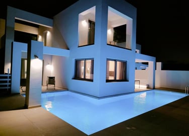 Modern luxury villa with a glowing L-shaped swimming pool and geometric architecture at night.